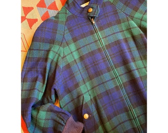 May include: A zip-up jacket featuring a blue and green plaid pattern. The jacket has a high collar with a single snap button closure, long sleeves with ribbed cuffs, and two front pockets, each secured with a single round tan snap button.