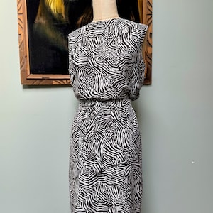 May include: A sleeveless dress with a black and white zebra print. The dress has a fitted bodice and a slightly flared skirt. It is belted at the waist.
