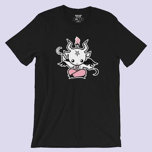 Pode incluir: Camiseta preta com um gráfico branco de um diabo de desenho animado com detalhes rosa. O diabo está usando um pentagrama e tem asas e chifres.