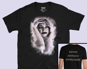May include: Black t-shirt with a graphic of a woman with a cross on her forehead and a painted mouth. The back of the shirt has the text "TOTAL FUCKING DARKNESS" in a gothic font.