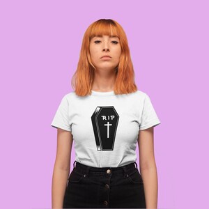 K&ouml;nnte beinhalten: Ein wei&szlig;es T-Shirt mit einer schwarz-wei&szlig;en Illustration eines Sarges mit dem Text "RIP" und einem Kreuz.