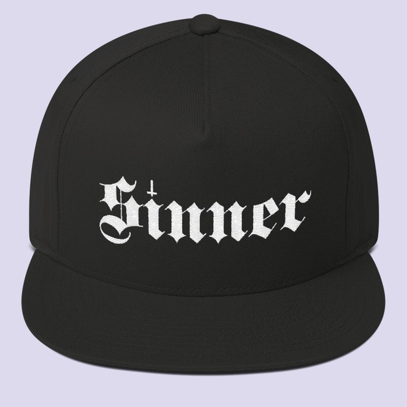 Puede incluir: Una gorra de b&eacute;isbol negra y blanca con un dise&ntilde;o bordado en blanco que dice "Sinner" en una fuente g&oacute;tica.