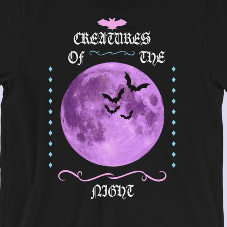 以下が含まれることがあります： 黒いTシャツに紫色の月とコウモリが描かれており、ピンク色の文字で「Creatures of the Night」と書かれています。