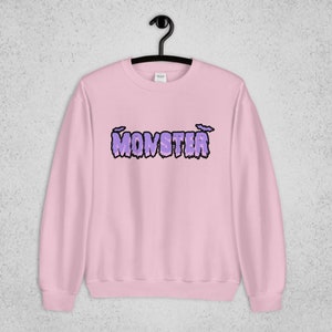 Pode incluir: Uma camisa de moletom rosa com um gr&aacute;fico roxo de "MONSTER" com letras pingando e morcegos acima do texto.