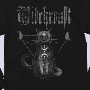 Pode incluir: Camiseta preta de manga comprida com uma ilustra&ccedil;&atilde;o de um gato preto e a palavra "WIRKRAFFT" em letras brancas. O gato est&aacute; rodeado por um tri&acirc;ngulo com luas crescentes em cada ponto.