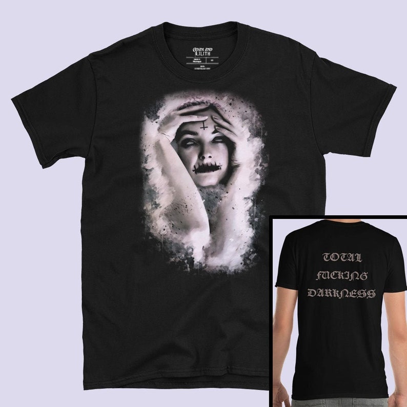 May include: Black t-shirt with a graphic of a woman with a cross on her forehead and a painted mouth. The back of the shirt has the text "TOTAL FUCKING DARKNESS" in a gothic font.