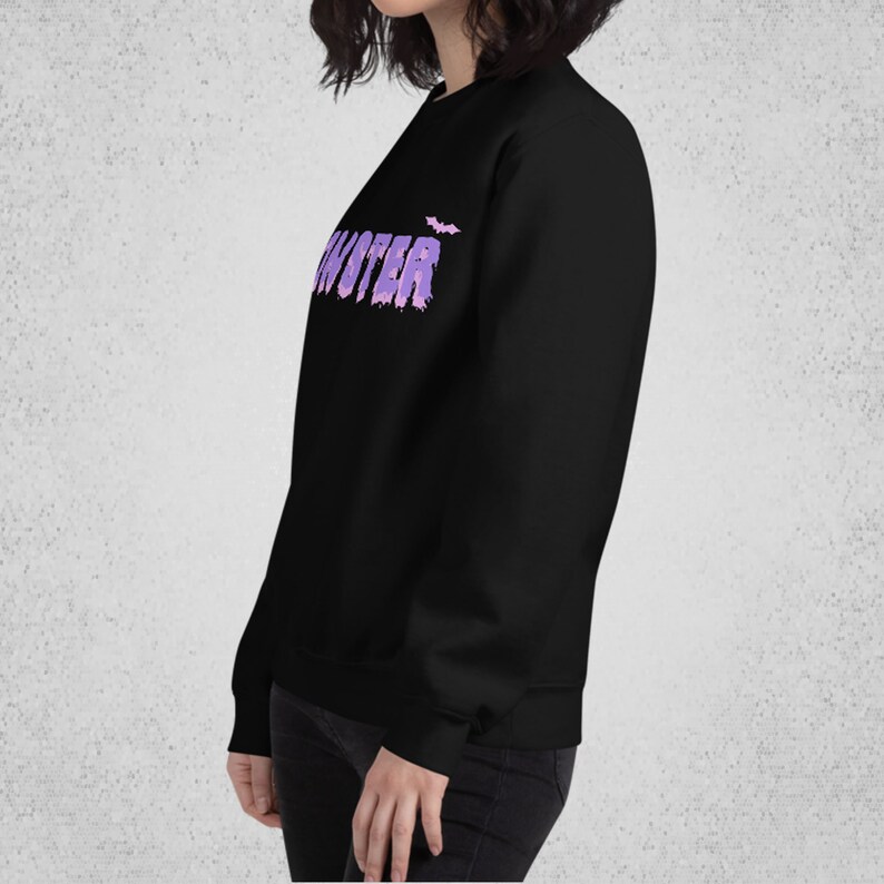 Pode incluir: Camisola de moletom preta com um gr&aacute;fico de "Monster" em roxo e rosa com um morcego acima do texto.