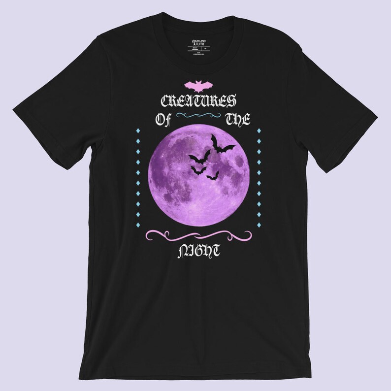 以下が含まれることがあります： 黒いTシャツに紫色の月とコウモリが描かれており、ゴシック体で「Creatures of the Night」という文字が書かれています。