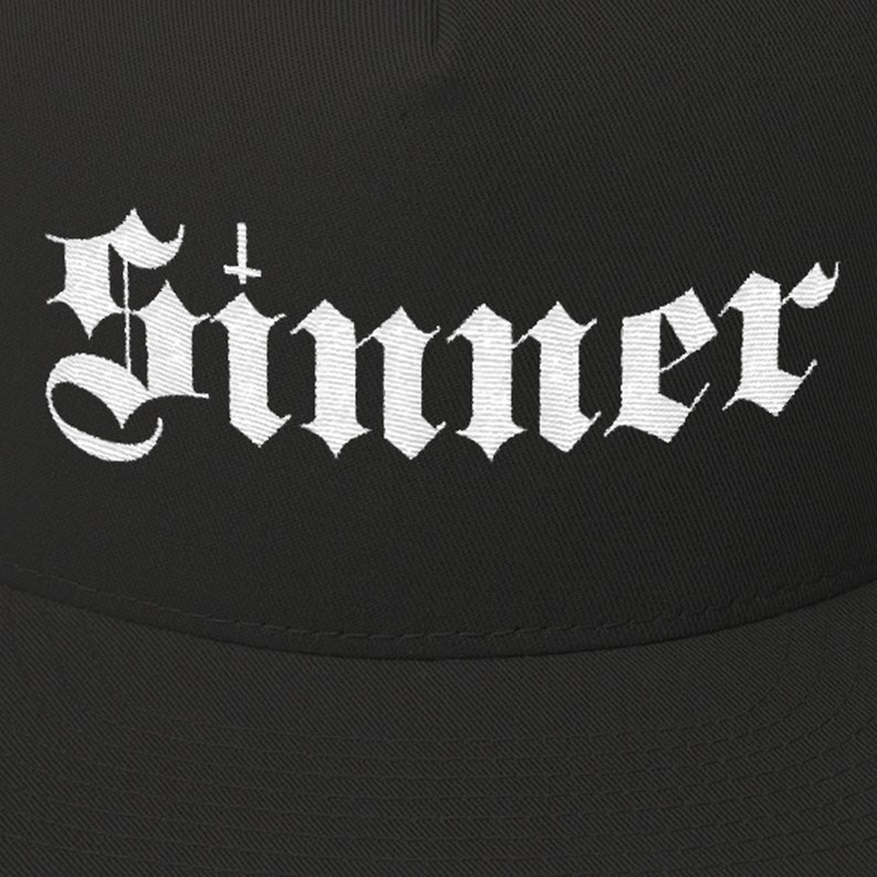 Puede incluir: Gorra de b&eacute;isbol negra con un dise&ntilde;o bordado en blanco que dice "Sinner" con una cruz sobre la primera letra.