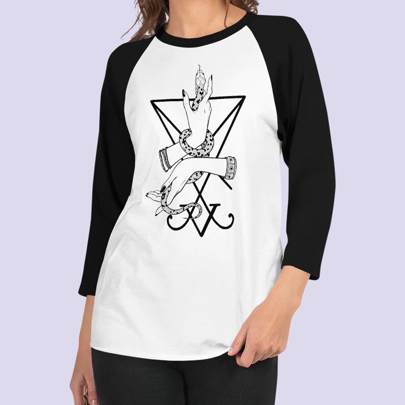 K&ouml;nnte beinhalten: Ein wei&szlig;es und schwarzes Baseball-T-Shirt mit einer schwarz-wei&szlig;en Illustration einer Hand, die eine Schlange in einem Dreieck h&auml;lt, mit dem Buchstaben 'X' darunter.