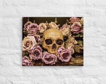 May include: A human skull surrounded by a wreath of pink roses. The skull is light brown and has visible eye sockets and teeth. The roses are arranged in a circle around the skull, with their petals overlapping.