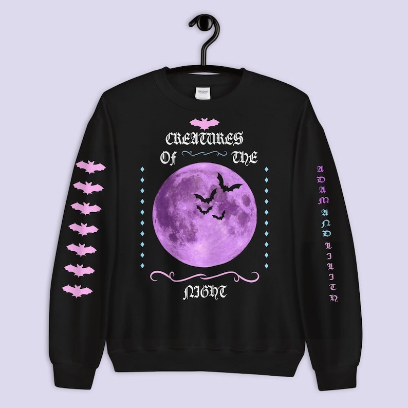 May include: Black sweatshirt with a purple moon and bats graphic. The text "Creatures of the Night" is printed on the front. The sleeves have a repeating pattern of bats.