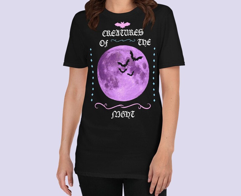 以下が含まれることがあります： ゴシック体で「Creatures of the Night」と書かれた、紫色の月とコウモリが描かれた黒いTシャツです。