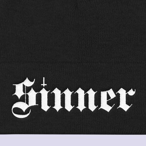 May include: Black beanie with a white embroidered "Sinner" logo in a gothic font.