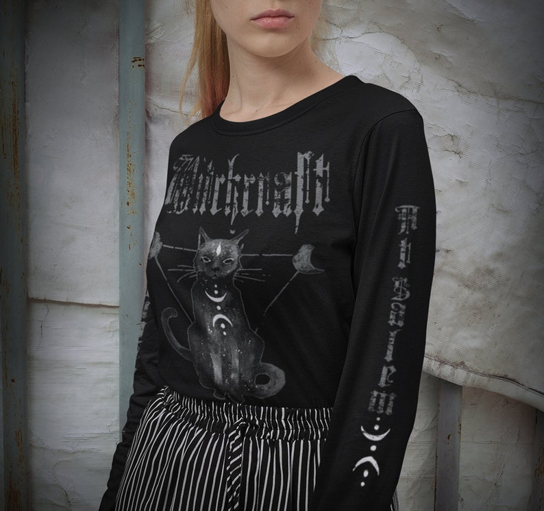 Pode incluir: Camiseta preta de manga comprida com uma estampa gr&aacute;fica de um gato preto com uma lua crescente e estrelas. O texto "Witchcraft" &eacute; impresso em uma fonte g&oacute;tica na frente da camiseta.