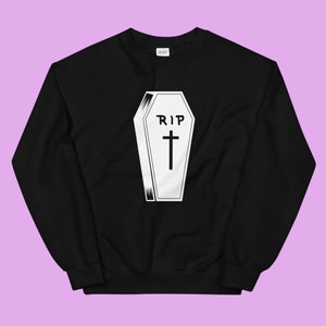 Może przedstawiać: Czarna bluza z białym nadrukiem przedstawiającym trumnę z krzyżem i napisem "RIP".