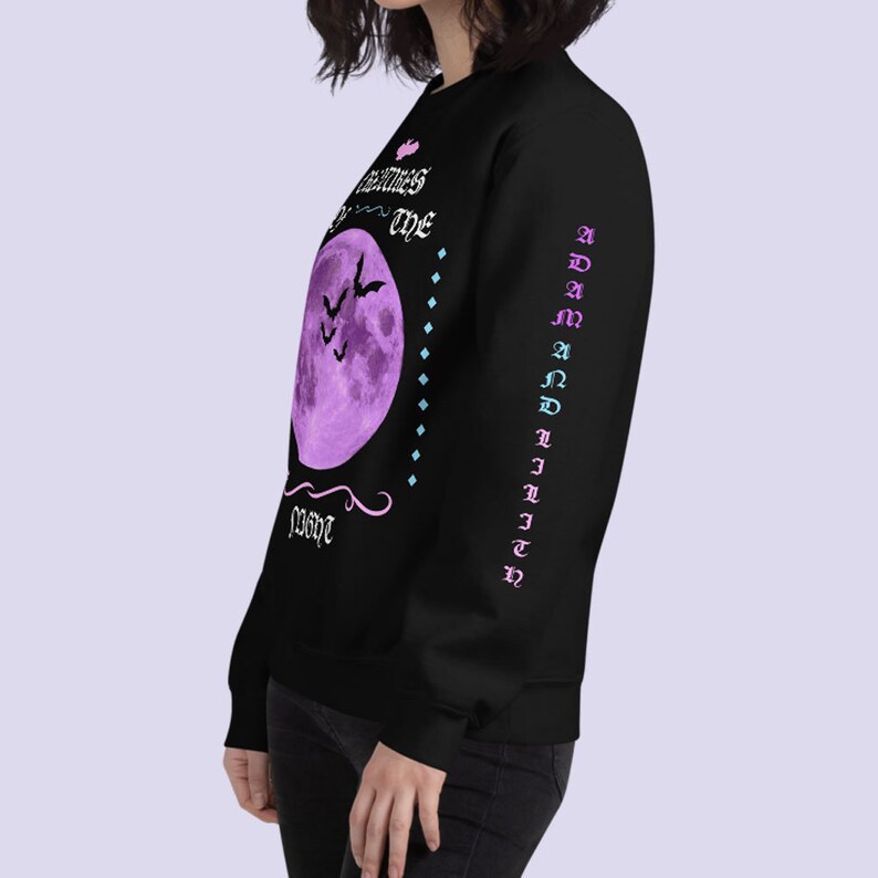 May include: Black long-sleeve sweatshirt with a purple moon and bats graphic. The text "Darkness is my home" is printed on the front. The text "ADAM AND LILITH" is printed on the sleeve.