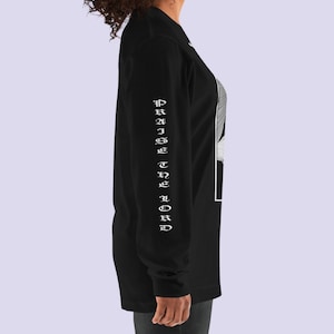 May include: Black long-sleeve shirt with a white graphic print on the front and the text "PRAISE THE LORD" printed vertically on the left sleeve.