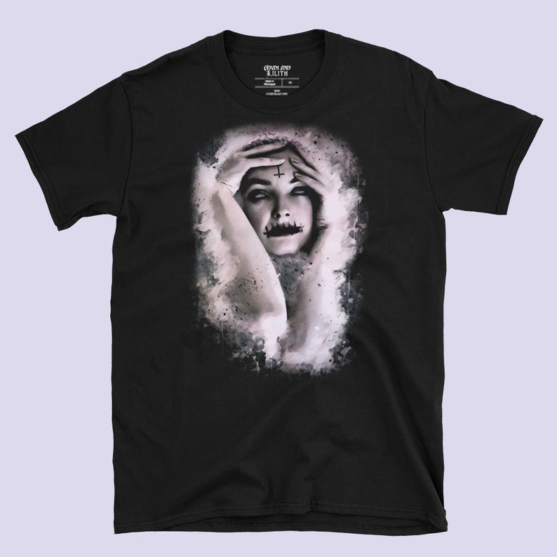 May include: Black t-shirt with a graphic print of a woman with a cross on her forehead and a painted mouth. The graphic is in a white and gray watercolor style.