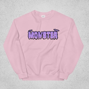 Pode incluir: Uma camisa de moletom rosa com um gr&aacute;fico roxo de "MONSTER" com letras pingando e morcegos acima do texto.