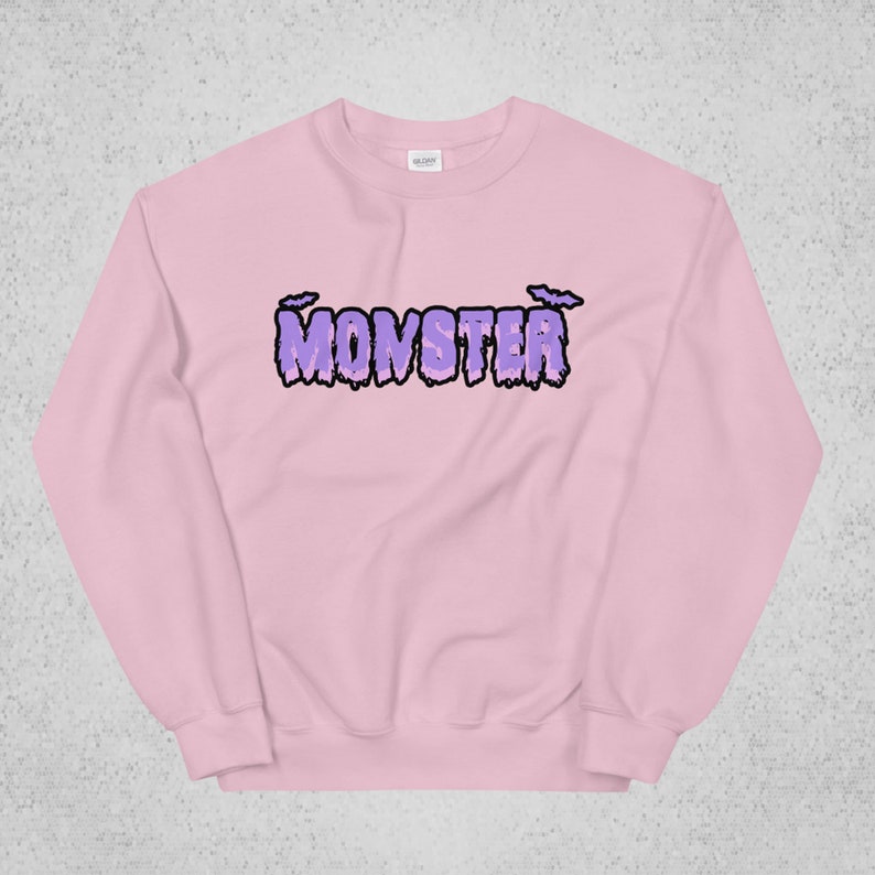 Pode incluir: Uma camisa de moletom rosa com um gr&aacute;fico roxo de "MONSTER" com letras pingando e morcegos acima do texto.