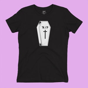 K&ouml;nnte beinhalten: Schwarzes T-Shirt mit einem wei&szlig;en Aufdruck eines Sarges mit dem Text "RIP" und einem Kreuz.