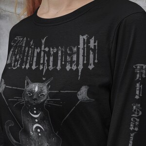 Pode incluir: Camiseta preta de manga comprida com uma estampa gr&aacute;fica de um gato preto com uma lua crescente e estrelas. O texto "Witchcraft" est&aacute; impresso em uma fonte g&oacute;tica na camiseta.