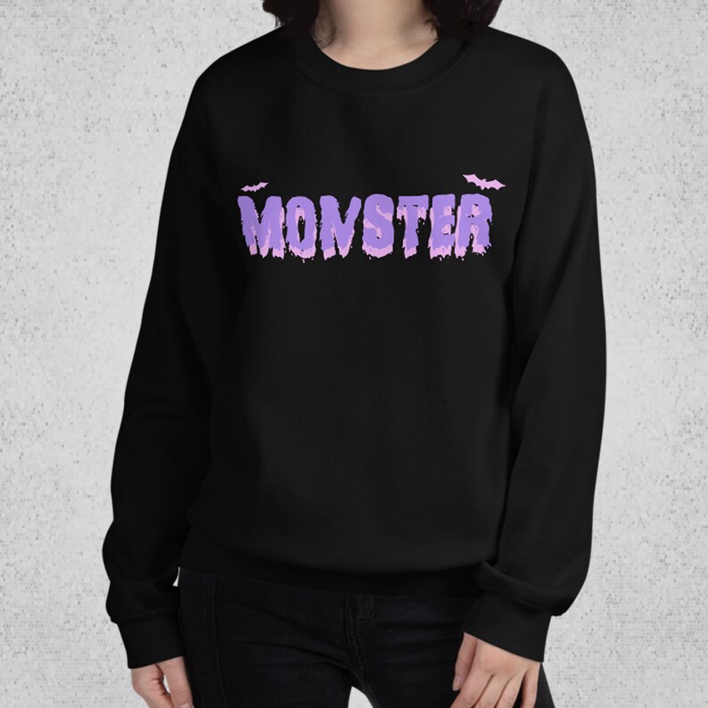Pode incluir: Camisola de moletom preta com um gr&aacute;fico roxo de "MONSTER" e dois morcegos pequenos acima do texto.