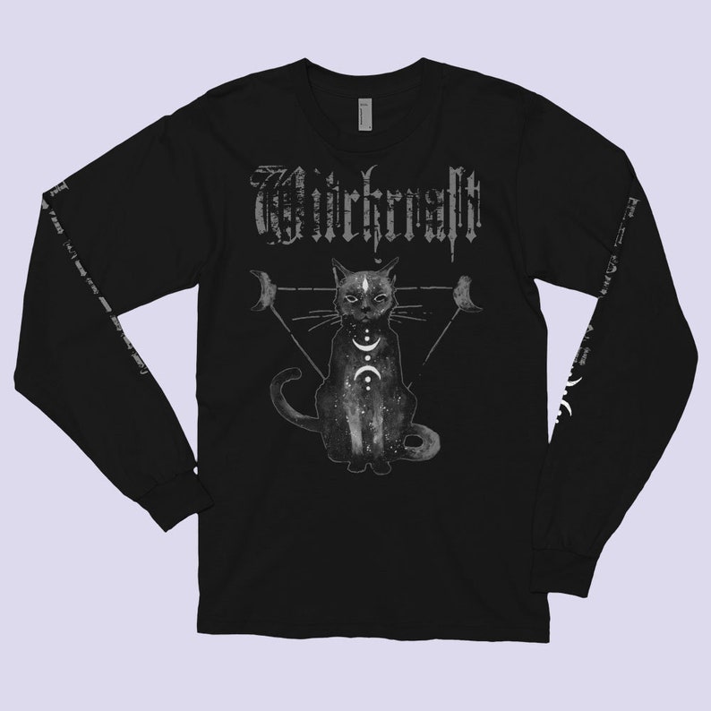 Pode incluir: Camiseta preta de manga comprida com um gr&aacute;fico branco de um gato sentado em um tri&acirc;ngulo com luas e a palavra "Witchcraft" acima do gato.