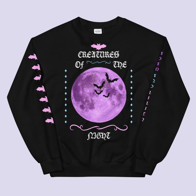 May include: Black sweatshirt with a purple moon and bats printed on the front. The text "Creatures of the Night" is printed in pink below the moon. The sleeves have a pink and white pattern.