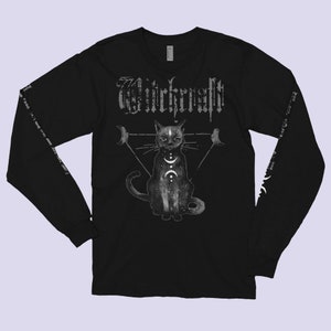 Pode incluir: Camiseta preta de manga comprida com um gr&aacute;fico de um gato preto sentado em um tri&acirc;ngulo com luas e a palavra "Witchcraft" acima do gato.