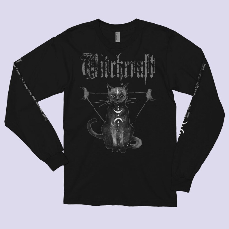 Pode incluir: Camiseta preta de manga comprida com um gr&aacute;fico de um gato preto sentado em um tri&acirc;ngulo com luas e a palavra "Witchcraft" acima do gato.