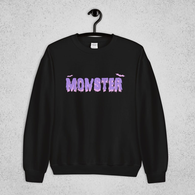 Pode incluir: Camisola de moletom preta com um gr&aacute;fico roxo de "MONSTER" e dois morcegos acima do texto.