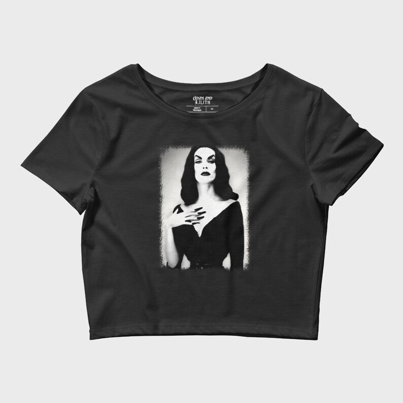 May include: Black cropped t-shirt with a graphic of a woman in a black dress with a white background. The graphic is in a vintage style and the woman has dark hair and dark makeup. The text "Coven and Lilith" is on the tag.