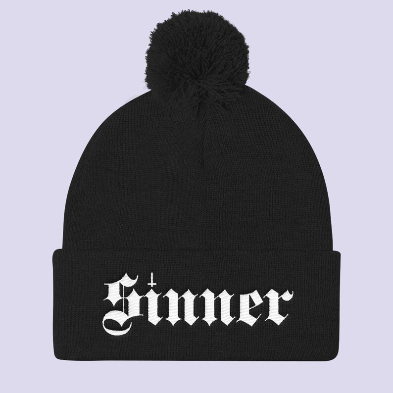 May include: Black beanie with a white pom pom and the word "Sinner" in white gothic lettering.