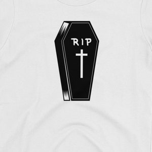 K&ouml;nnte beinhalten: Schwarz-wei&szlig;-Illustration eines Sarges mit den Worten "RIP" und einem Kreuz.