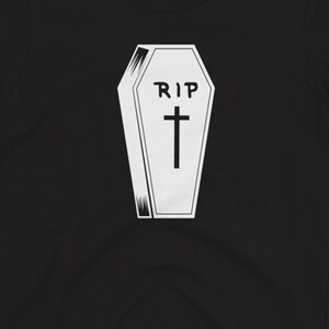 K&ouml;nnte beinhalten: Ein schwarzes T-Shirt mit einer wei&szlig;en Grafik eines Sarges mit dem Text "RIP" und einem Kreuz.