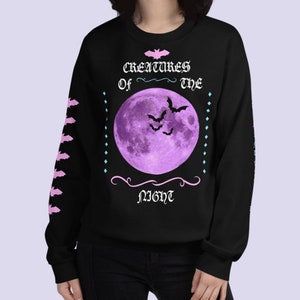 May include: Black sweatshirt with a purple moon and bats graphic. The text "Creatures of the Night" is printed in pink and white.