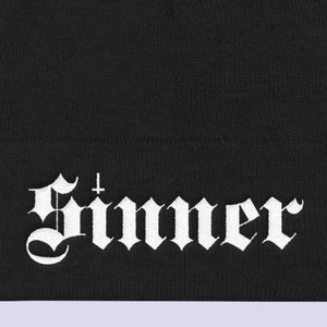 May include: Black beanie with a white embroidered "Sinner" logo in a gothic font.