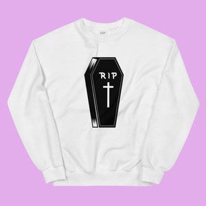 Może przedstawiać: Biała bluza z czarno-białym nadrukiem przedstawiającym trumnę z napisem "RIP" i krzyżem.