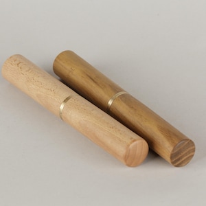 Puede incluir: Dos palilleros de madera. Uno es de madera de color claro, el otro de madera más oscura. Ambos tienen una banda dorada en el medio. Los soportes son cilíndricos y parecen hechos a mano.