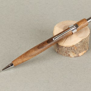 May include: A wooden mechanical pencil with a silver clip and tip. The pencil is resting on a small wooden log.