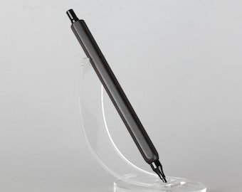 May include: A sleek black pen with a hexagonal barrel and a click-top mechanism, positioned at an angle within a clear, curved acrylic display stand that holds the writing instrument securely in place for a clear view of its design.