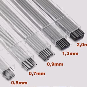 Puede incluir: Seis tubos de plástico transparente que contienen minas de lápiz de grafito de diferentes tamaños. Las minas están ordenadas de la más pequeña a la más grande, con los tamaños indicados en milímetros: 0,5 mm, 0,7 mm, 0,9 mm, 1,3 mm y 2,0 mm.