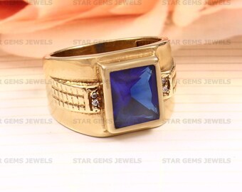 May include: A gold ring with a large, square, blue gemstone and two smaller, round, white gemstones on the side. The ring has a textured band.