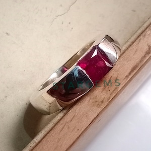 Puede incluir: Un anillo de plata con dos piedras preciosas cuadradas rojas engastadas en la banda.