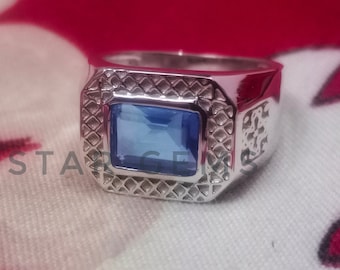 May include: A silver ring with a blue gemstone set in a square shape. The ring has a textured band.