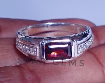 May include: A silver ring with a red gemstone and small clear gemstones on the band.