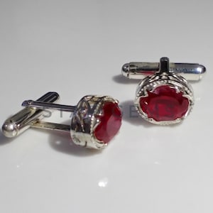 May include: A pair of silver cufflinks with red gemstone accents. The cufflinks have a detailed design and are a classic accessory.