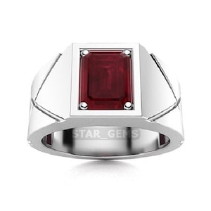 Puede incluir: Un anillo de plata con una piedra preciosa roja de talla esmeralda engastada en un bisel cuadrado. El anillo tiene un diseño simple y moderno y está grabado con el texto "STAR_GEMS".